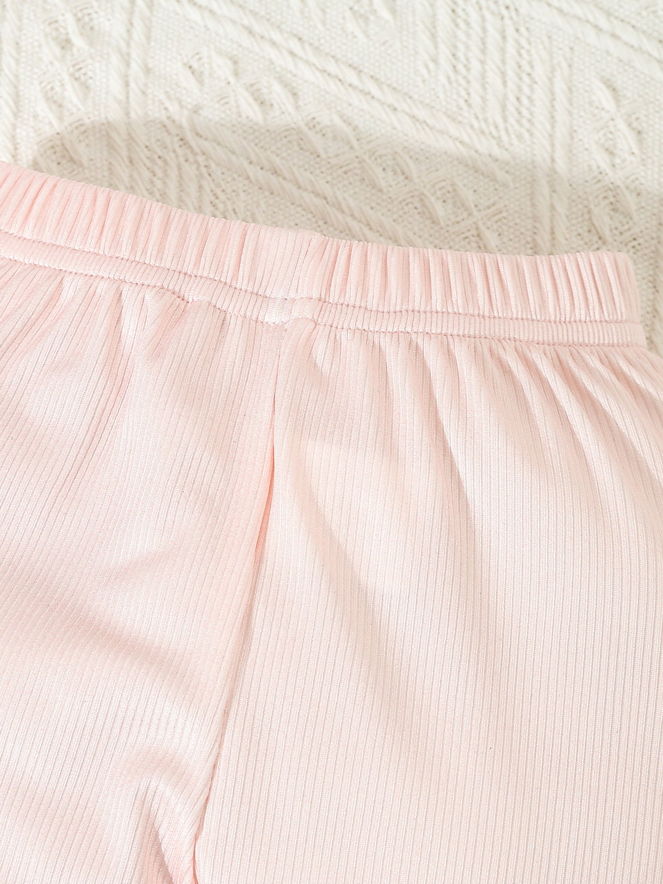 Close-up of pink ribbed pants with a textured white background
