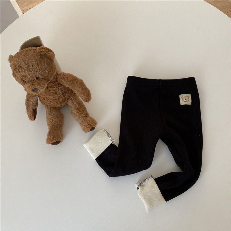 Brown teddy bear and black pants with white cuffs on a light gray surface