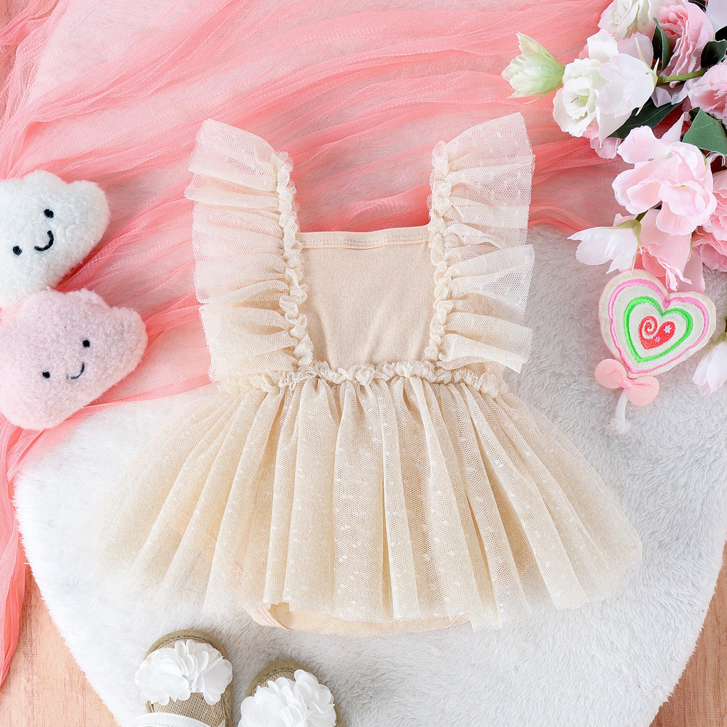 Beige baby dress with ruffled details on a pink and white floral background