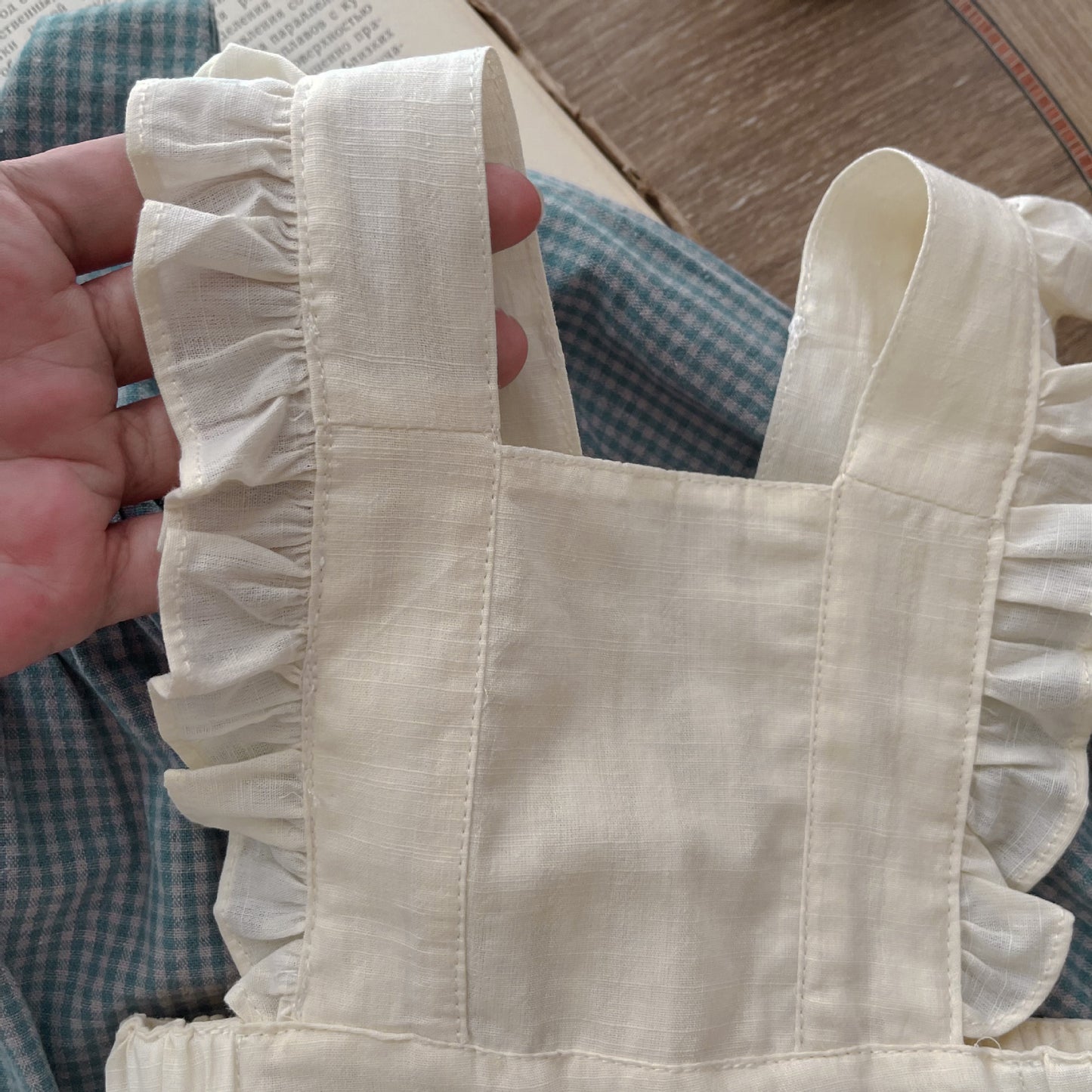 Beige tote bag with ruffled handles held by a person wearing a green checkered shirt.