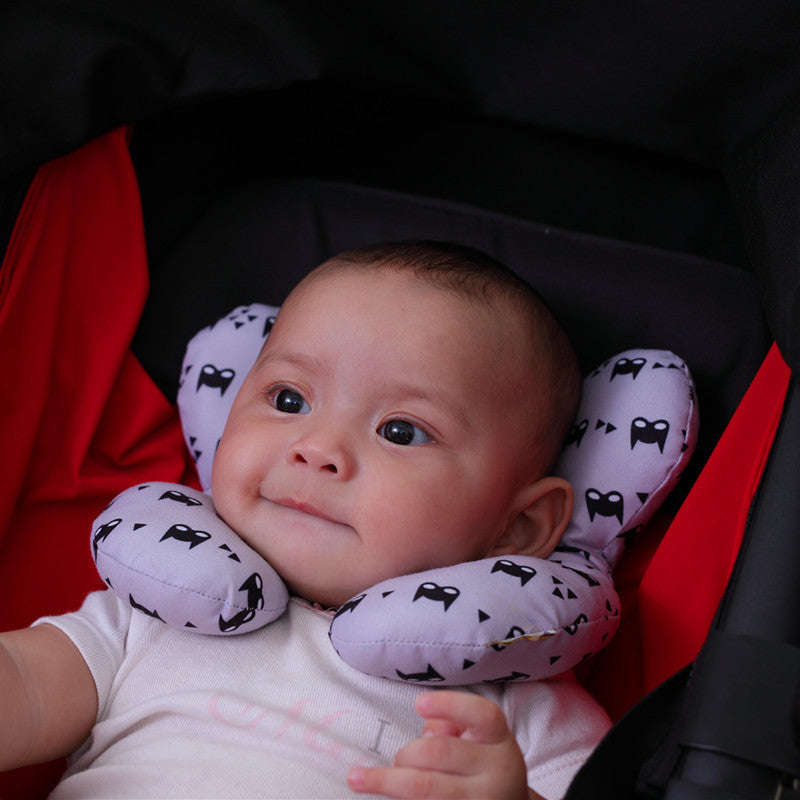Baby wearing a purple neck pillow with black cat patterns in a car seat.