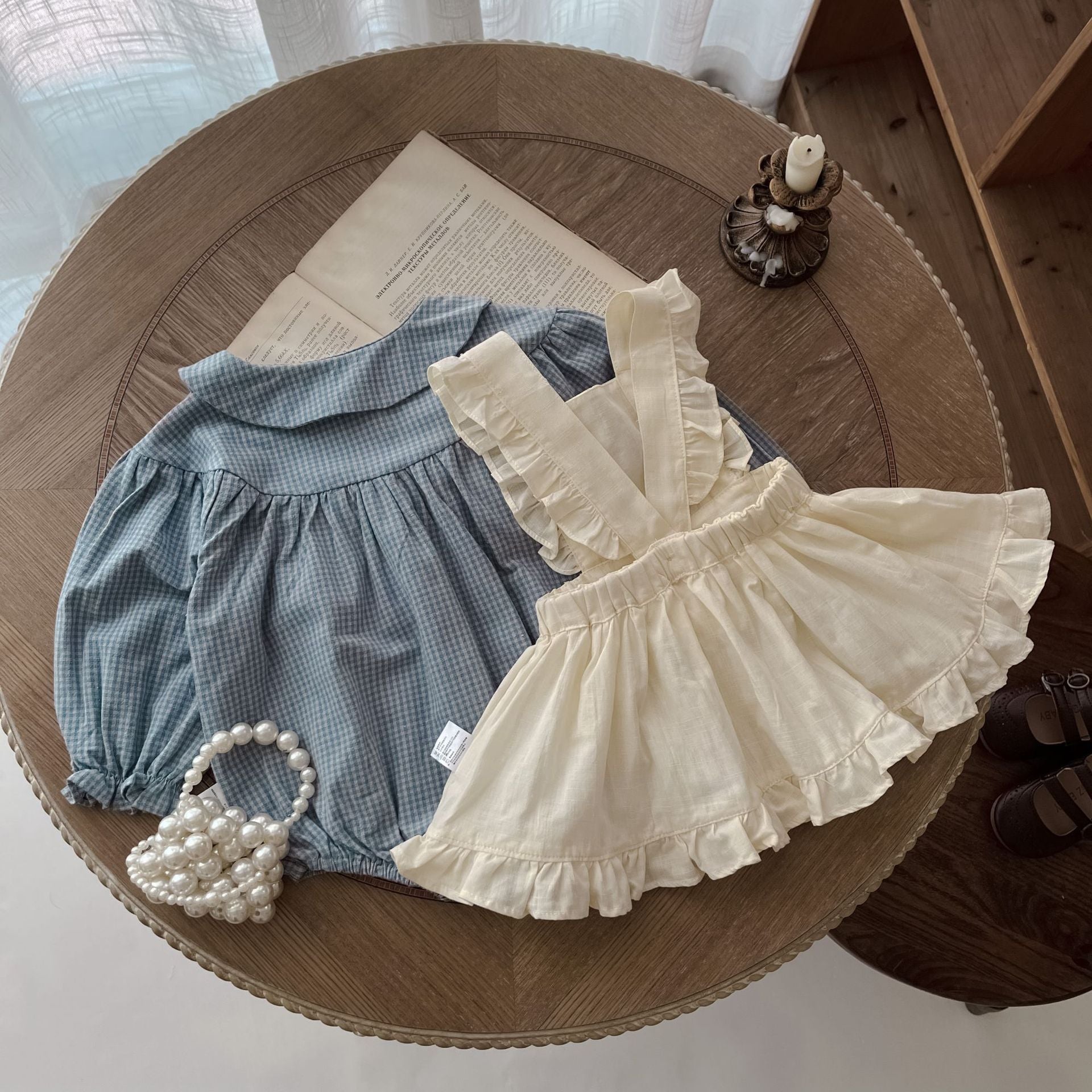 Children's outfit with blue checkered romper and white ruffled dress on a wooden surface.