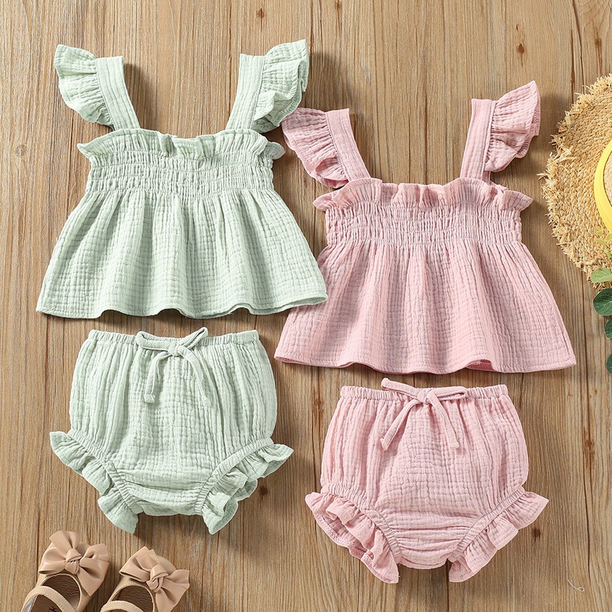 Set of matching baby outfits with ruffled tops and bloomers on a wooden surface.