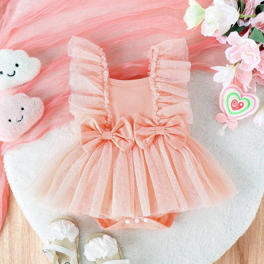 Pink baby romper with ruffles and a bow, surrounded by flowers and toys on a light surface.