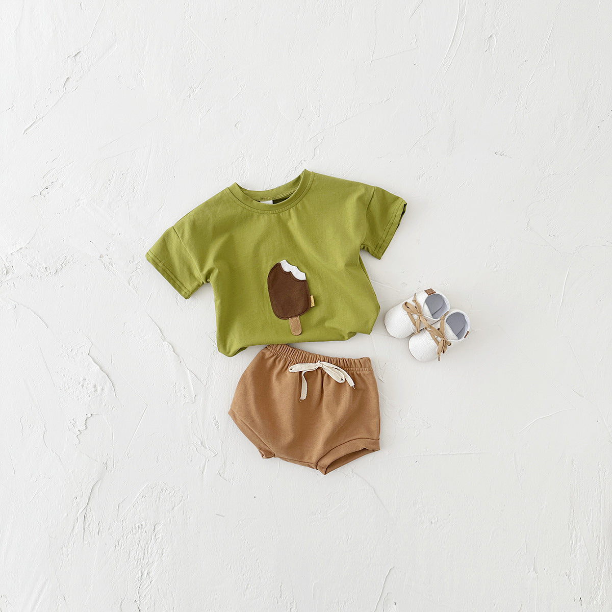 Children's green shirt with brown shorts and shoes on a white background