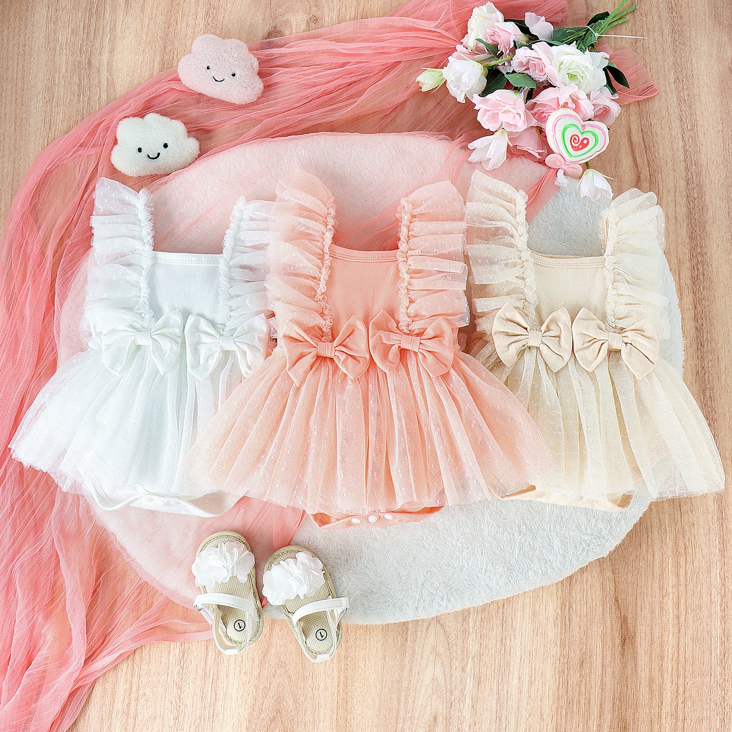 Three baby dresses in white, pink, and beige with matching shoes on a pink fabric background.
