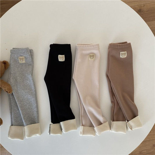 Four pairs of baby leggings in gray, black, pink, and brown on a white surface.