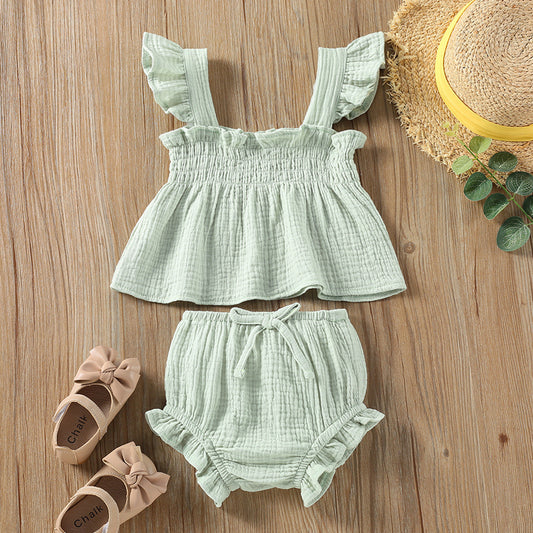 Mint green baby outfit with top and shorts on a wooden surface, accompanied by shoes and a hat.