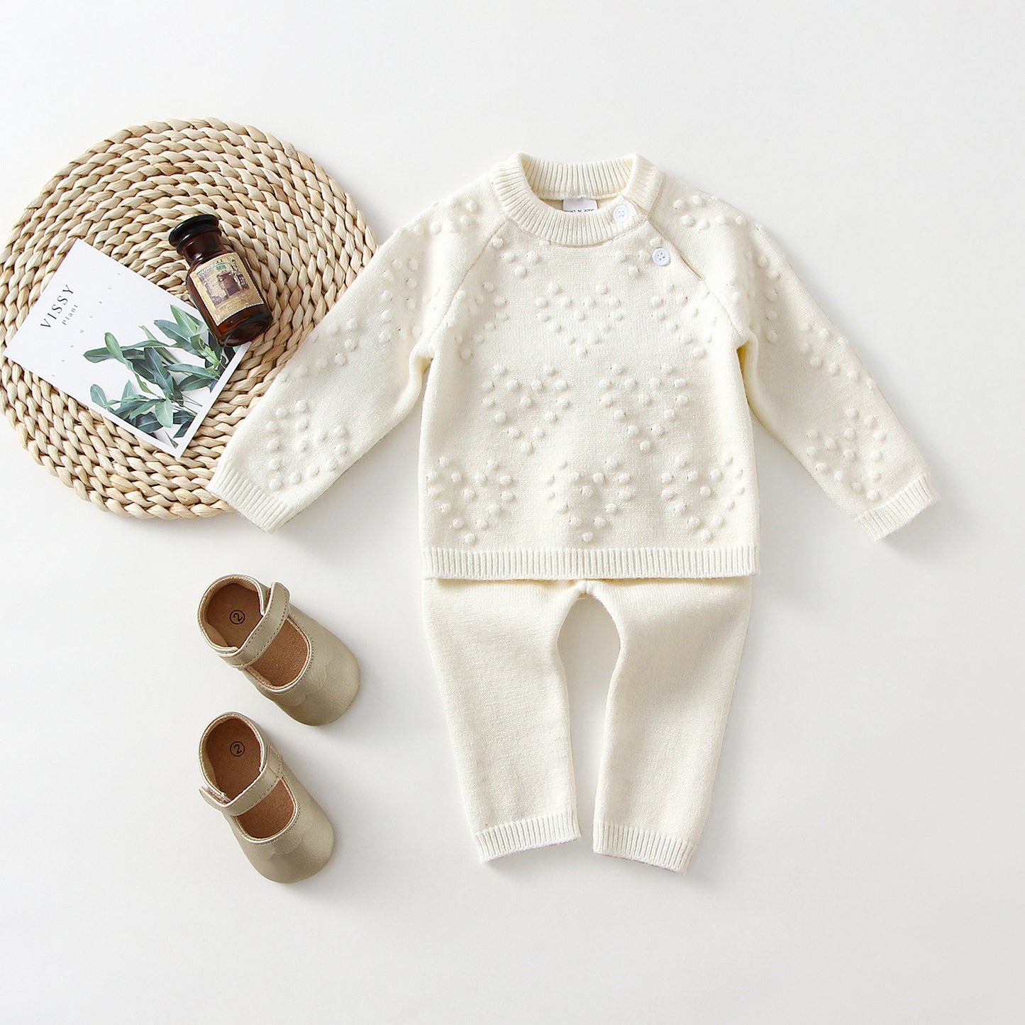 White knitted sweater and pants set with baby shoes on a light background
