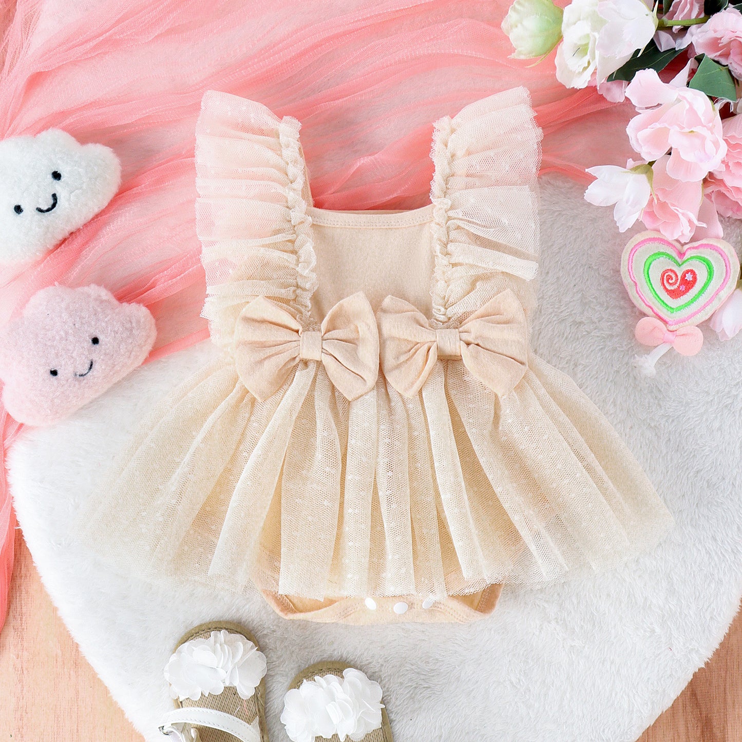 Baby dress with ruffles and bows on a pink and white background with toys and flowers.