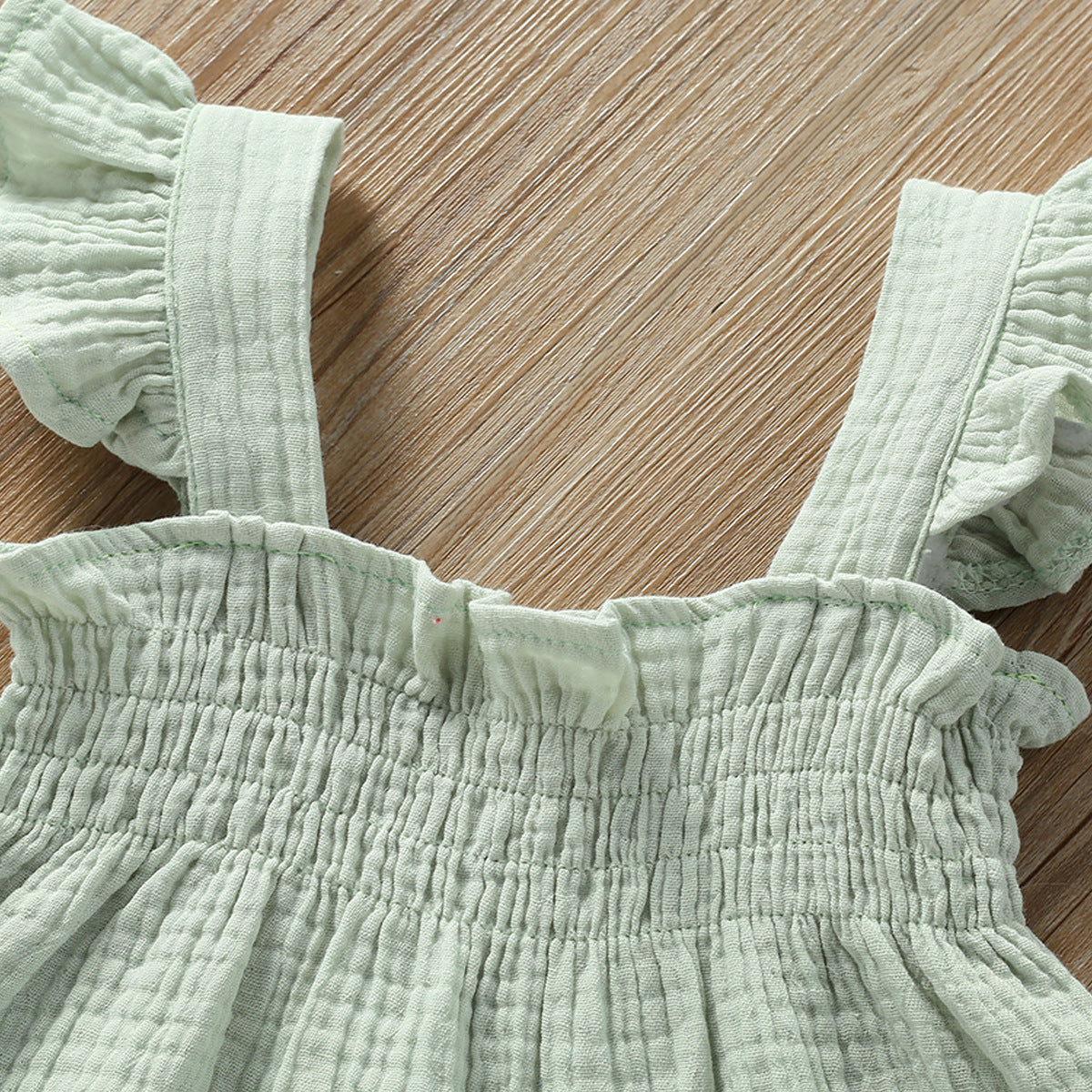 Light green dress with ruffled straps on a wooden surface