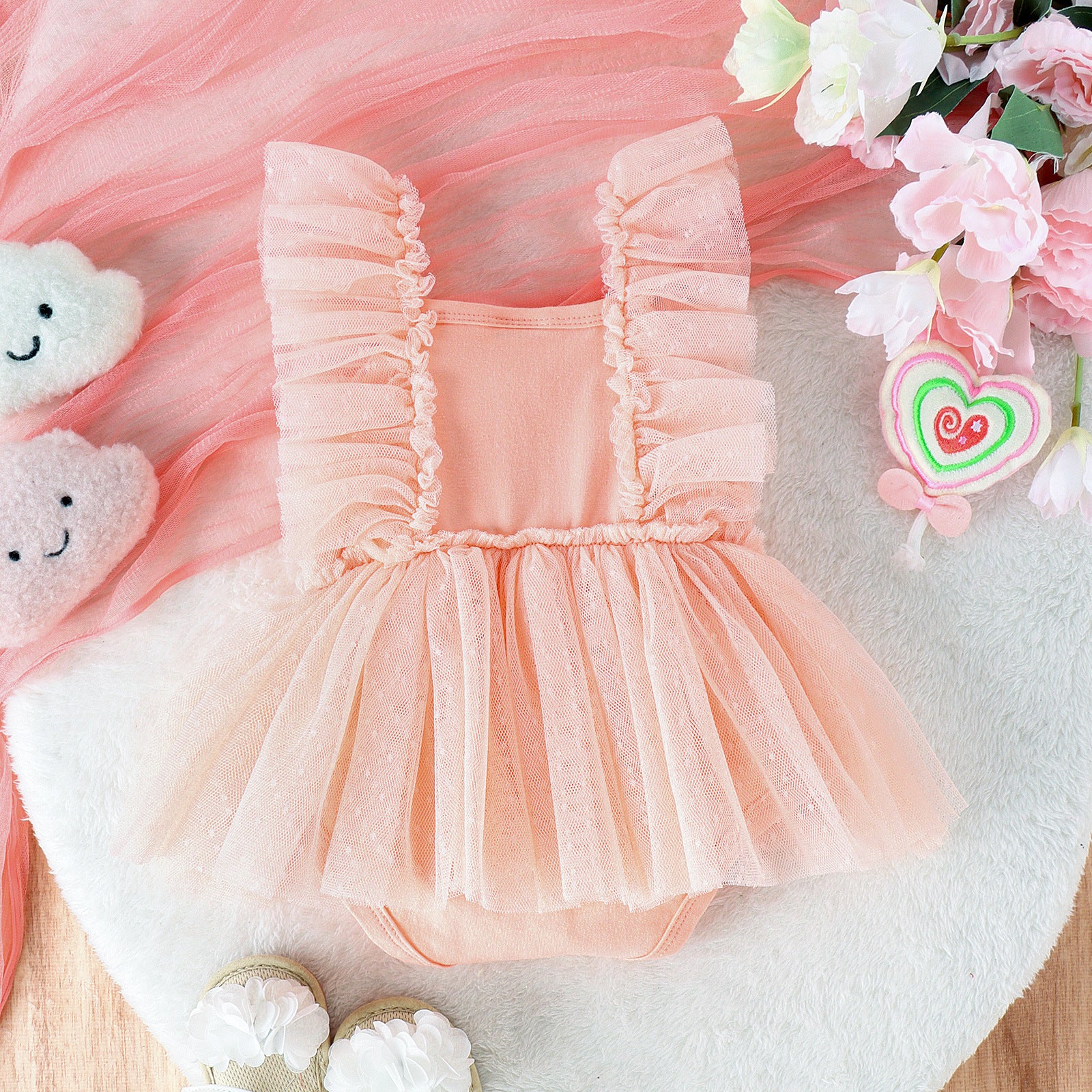 Pink ruffled dress on a soft pink fabric background with flowers and toys.