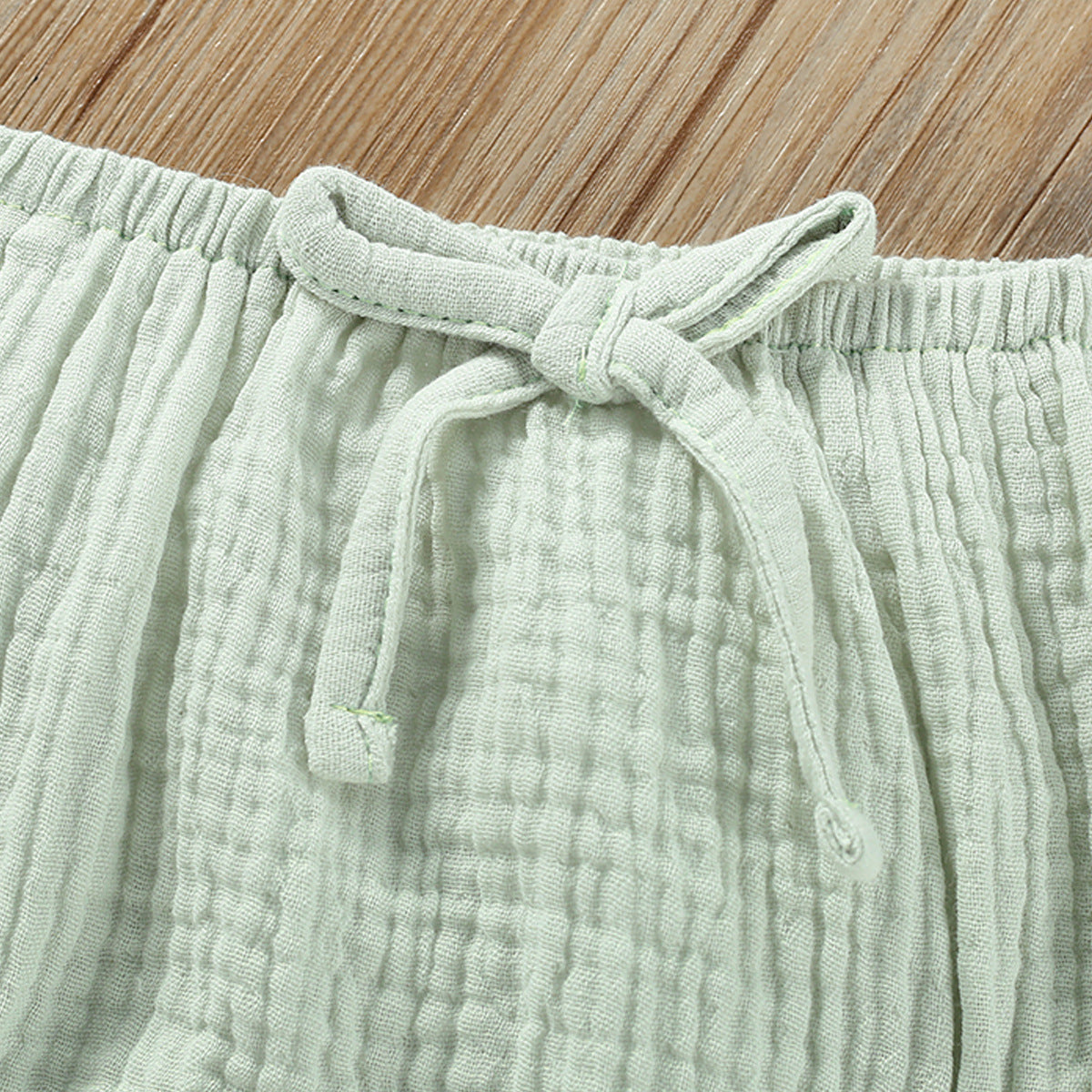 Light green textured pants with a tie detail on a wooden surface