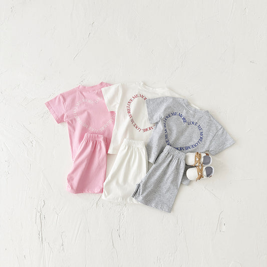 Children's clothing set with pink t-shirt, white dress, gray pants, and shoes on a light background