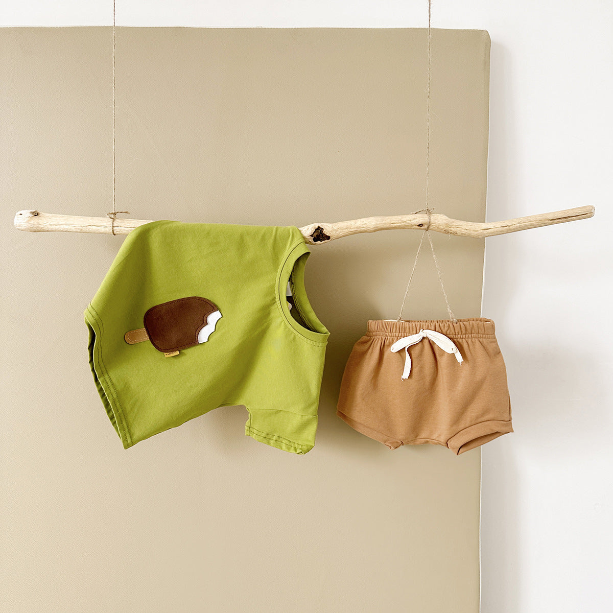 Green sleeveless top with a brown patch and brown shorts hanging on a branch against a beige wall.