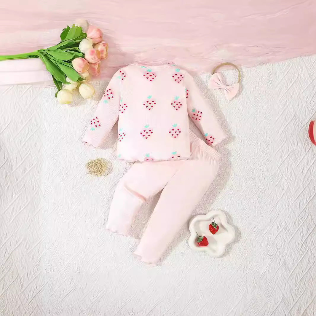 Pink baby outfit with floral patterns on a textured surface with flowers and a toy.