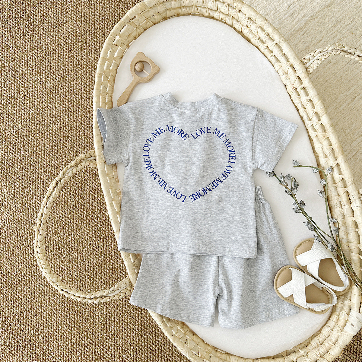 Gray baby outfit with text on a white surface in a wicker basket.